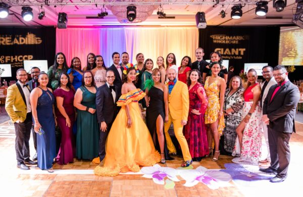 Group photo of 30+ Latino Connection team members dressed up for the ball and posing with an entertainer earing a brigh, yellow and flowy dress.